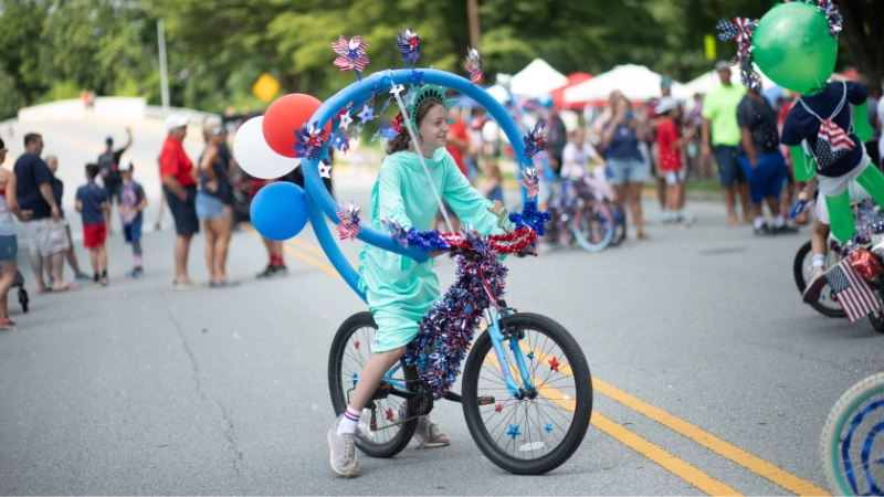 A young girl dressed as the Statue of Liberty riding a decorated bicycle